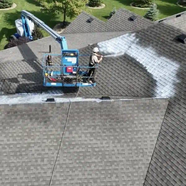 A boom lift applying Reactiv8 treatment across a shingle roof